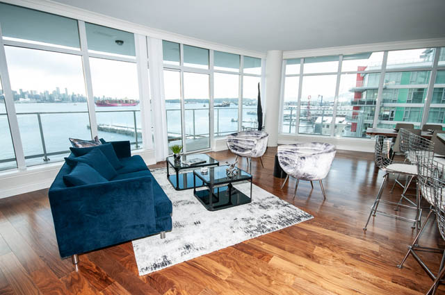 Bright living room with hardwood floors, city view, and modern furniture. - 702 - 185 Victory Ship Way, North Vancouver