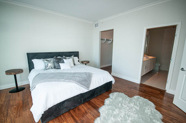 Spacious bedroom with hardwood floors, large bed, and closet access. - 702 - 185 Victory Ship Way, North Vancouver