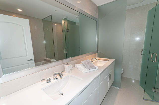 Spacious bathroom with large mirror, modern sink, and glass shower. - 702 - 185 Victory Ship Way, North Vancouver