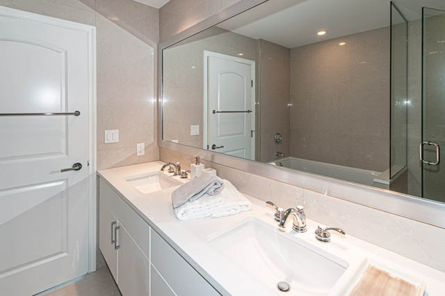 Furnished bathroom with modern sink, large mirror, and beige walls. - 702 - 185 Victory Ship Way, North Vancouver