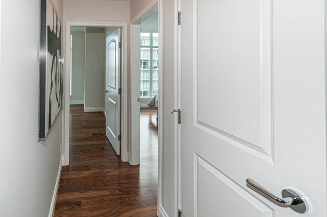 Bright hallway with white walls and wooden flooring, leading to a furnished living area. - 702 - 185 Victory Ship Way, North Vancouver