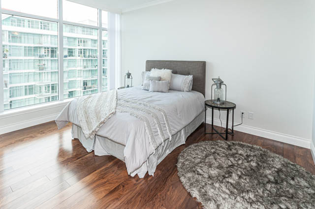 Bright bedroom with hardwood floors, city view, and cozy bedding. - 702 - 185 Victory Ship Way, North Vancouver