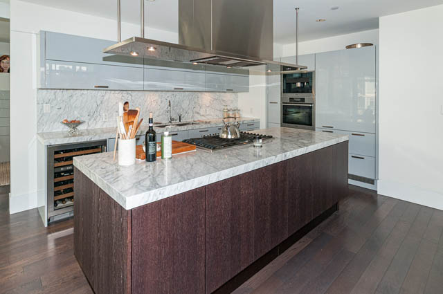 Bright kitchen with marble countertops and dark wood cabinets, featuring a modern stove and stainless steel appliances.
