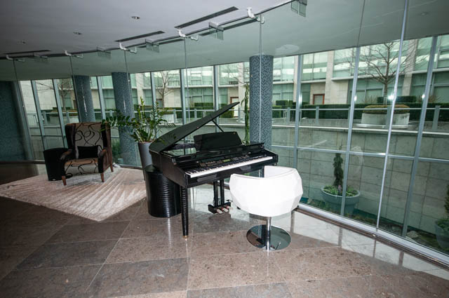 Furnished living room with grand piano, large windows, and city view. - 601 - 1560 Homer Mews, Vancouver Downtown