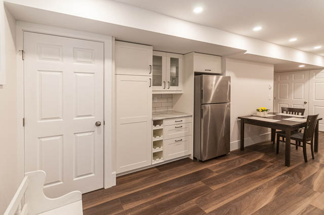 Bright kitchen with white cabinetry and stainless steel appliances, hardwood floors, and a dining area. - SUITE - 2806 Munday Place, North Vancouver