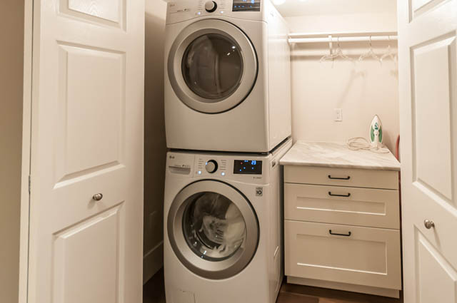 Bright laundry room with stacked washer and dryer, white cabinets, and ironing board. - SUITE - 2806 Munday Place, North Vancouver