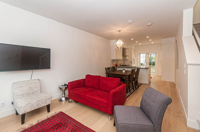 Open-concept living space with red couch, hardwood floors, and a kitchen in the background. - 9 - 1133 Ridgewood Drive, North Vancouver