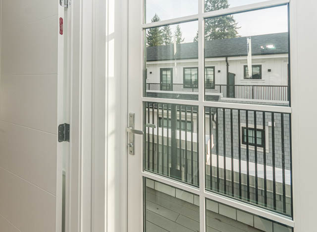 Bright living room with large windows showing a modern townhouse exterior and balcony view. - 9 - 1133 Ridgewood Drive, North Vancouver
