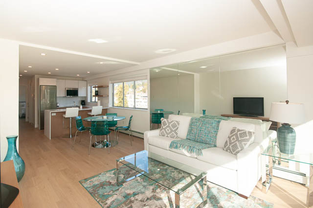 Bright living room with hardwood floors and a city view, featuring a glass coffee table and modern furniture. - 708 - 150 24th St, West Vancouver
