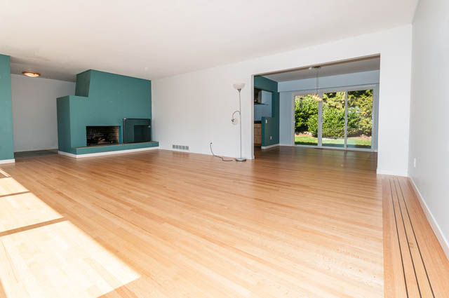 Spacious living room with hardwood floors and a teal fireplace, leading to a patio with a view. - 4037 Ripple Road, West Vancouver