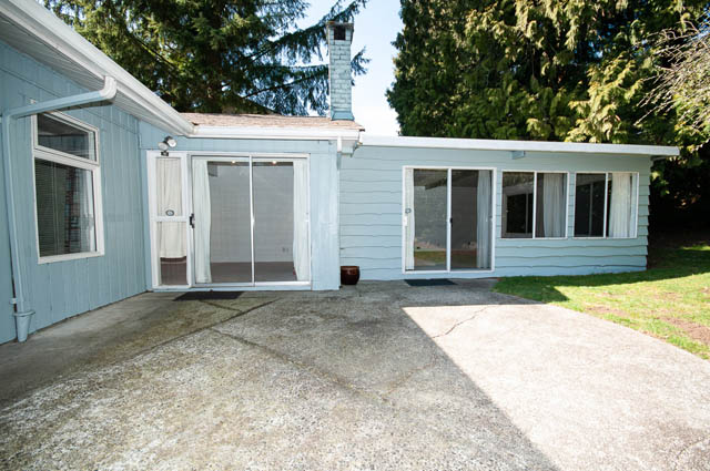 Bright living room with sliding glass doors leading to a patio, surrounded by greenery. - 4037 Ripple Road, West Vancouver