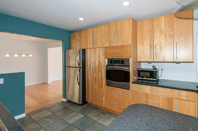 Bright kitchen with wooden cabinets, granite countertops, and hardwood floors. - 4037 Ripple Road, West Vancouver