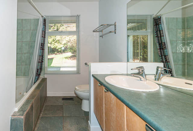 Bathroom with green countertops and wooden cabinets, large window view. - 4037 Ripple Road, West Vancouver