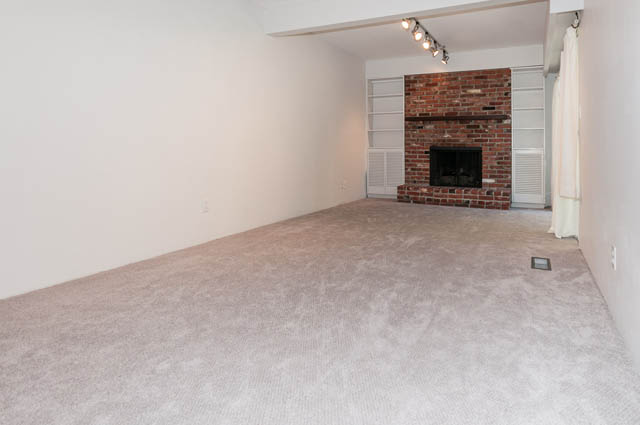 Living room with exposed brick fireplace and carpeted floor. - 4037 Ripple Road, West Vancouver