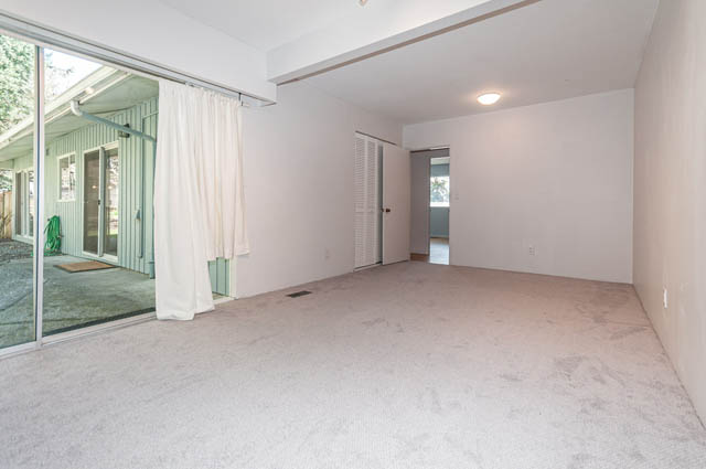 Spacious living room with sliding glass doors leading to a patio, white walls, and a cozy corner. - 4037 Ripple Road, West Vancouver