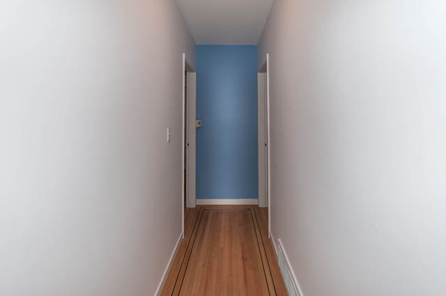 Narrow hallway with blue accent wall and wooden flooring. - 4037 Ripple Road, West Vancouver