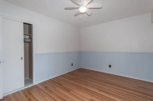 Bright bedroom with hardwood floors and white walls, featuring a closet and ceiling fan. - 4037 Ripple Road, West Vancouver