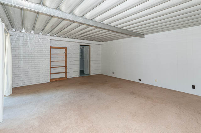 Bright living room with exposed ceiling beams and white brick accent wall. - 4037 Ripple Road, West Vancouver