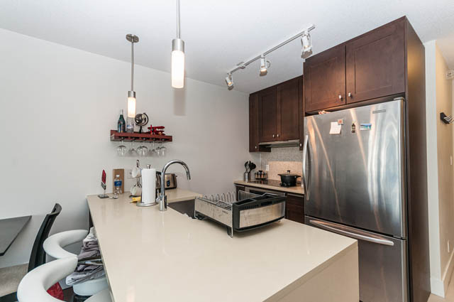 Modern kitchen with sleek stainless steel appliances and dark wood cabinets, featuring a large island and pendant lighting.