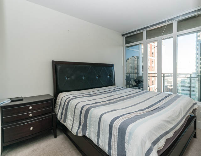 Spacious 1-bedroom + den condo with a large bed, striped bedding, and a stunning city view from the sliding glass doors.