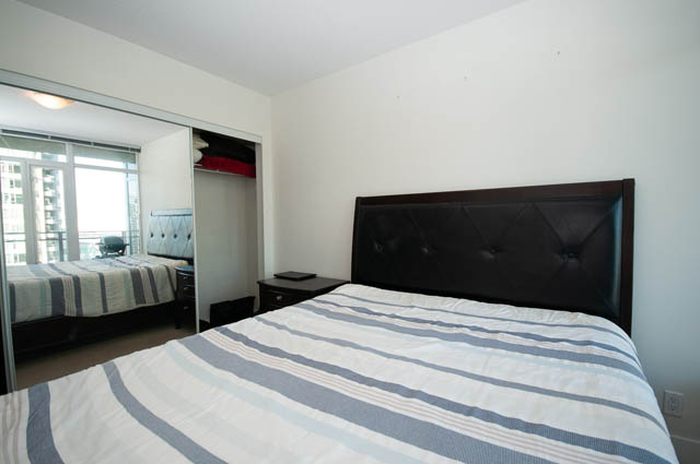 Spacious 1-bedroom + den condo with modern furniture, large windows offering city views, and a cozy bedroom setup.