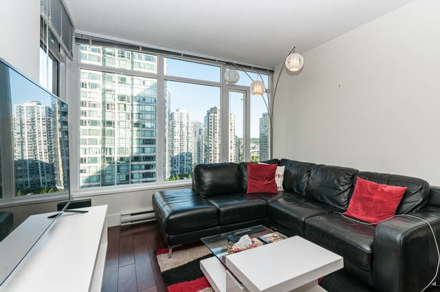Spacious living room with black leather sectional, red throw pillows, and cityscape view through large windows.