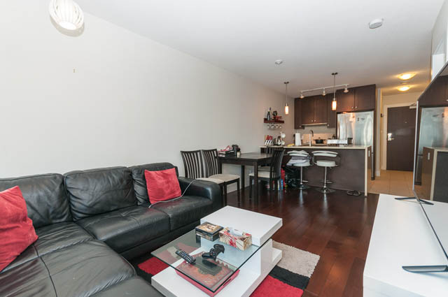 Spacious living room with black leather couch, red accents, and hardwood floors. - 1607 - 888 Homer St, Vancouver Downtown