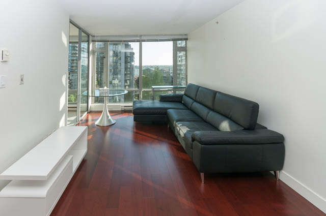 Spacious living room with hardwood floors, a modern black sectional, and a city view through large windows. - 903 -1255 Seymour St, Vancouver Downtown