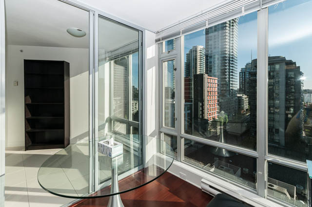 Spacious living room with large windows offering a stunning city view, featuring a sleek glass table and modern furnishings.