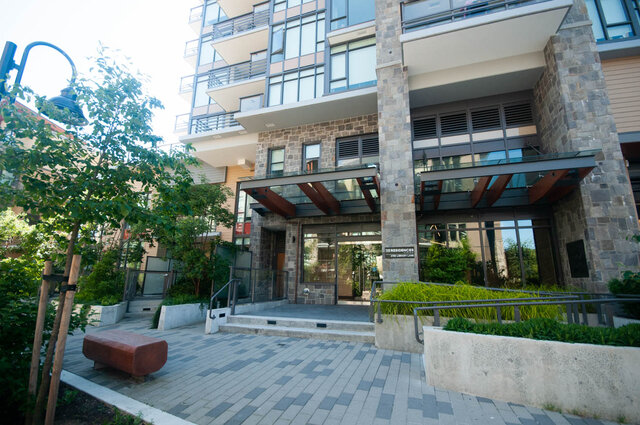 The entrance features a glass canopy, stone columns, steps, and landscaping. - 203 -2785 Library Lane, North Vancouver