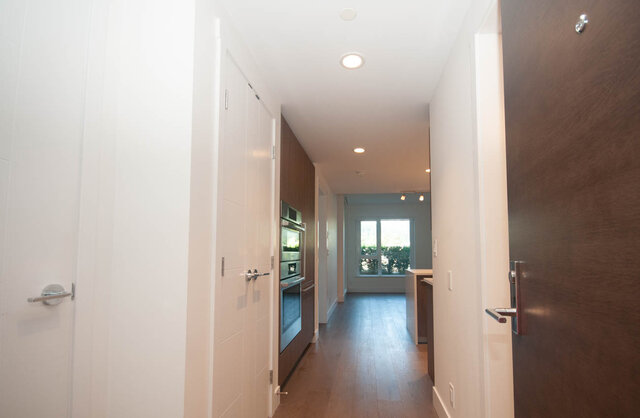 The hallway has hardwood floors, recessed lighting, and doors on both sides. - 203 -2785 Library Lane, North Vancouver