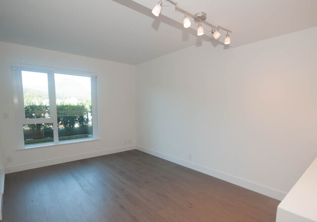 This is a bedroom with a window, hardwood floors, and track lighting. - 203 -2785 Library Lane, North Vancouver