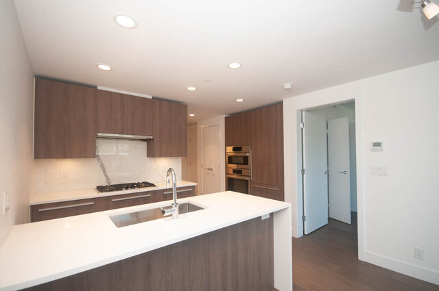 The kitchen features wooden cabinets, a stainless steel sink, a gas stove, and stainless steel appliances. - 203 -2785 Library Lane, North Vancouver