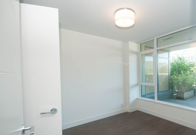 This is a bedroom with a ceiling light, large windows, and hardwood floors. - 203 -2785 Library Lane, North Vancouver