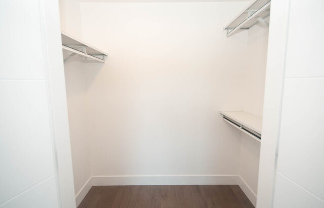 This is a storage locker with white shelves, hanging rods, and wooden flooring. - 203 -2785 Library Lane, North Vancouver