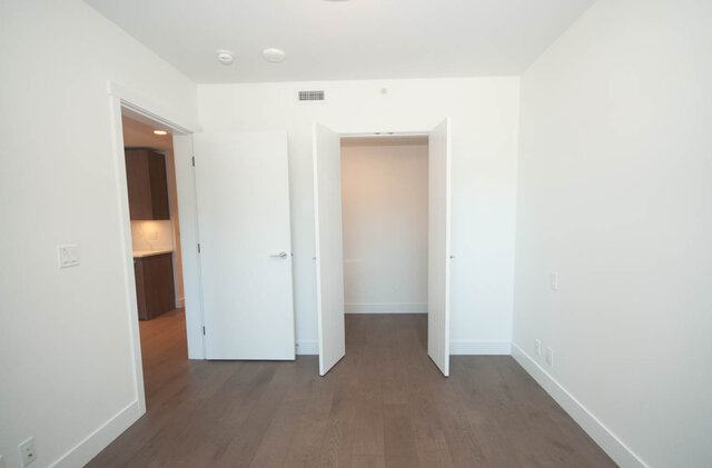 This is a hallway with white walls, hardwood floors, and multiple doorways leading to other rooms. - 203 -2785 Library Lane, North Vancouver