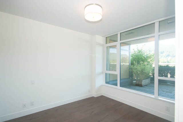 This is a bedroom with hardwood floors, large windows, and a ceiling light. - 203 -2785 Library Lane, North Vancouver