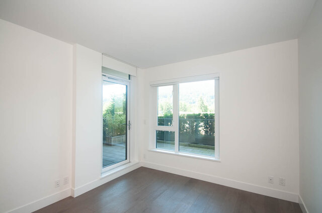 This is a bedroom with white walls, hardwood floors, a sliding glass door, and a window. - 203 -2785 Library Lane, North Vancouver