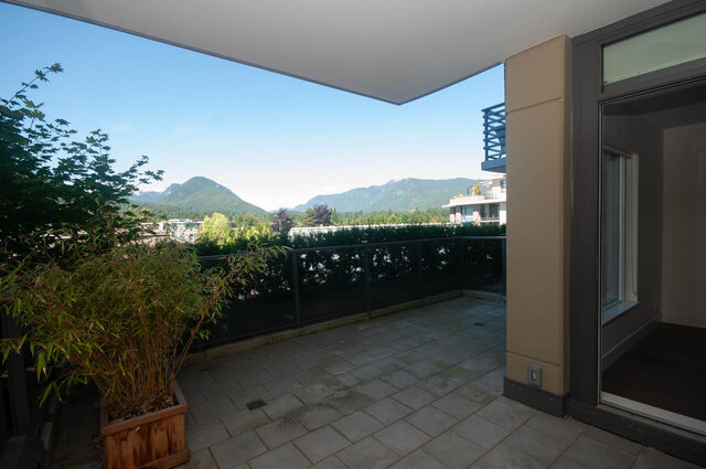 The balcony features a potted plant, stone tile flooring, a railing, and a view of mountains and trees. - 203 -2785 Library Lane, North Vancouver