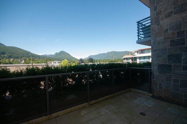 The balcony features a railing, mountain view, and greenery in the background - 203 -2785 Library Lane, North Vancouver