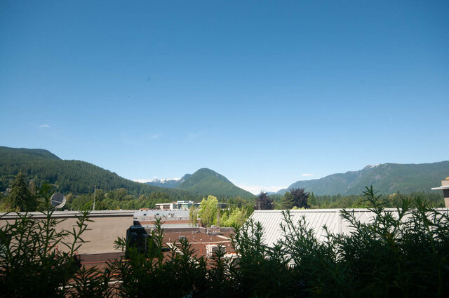 The view shows distant mountains, greenery, and city buildings under a clear blue sky - 203 -2785 Library Lane, North Vancouver