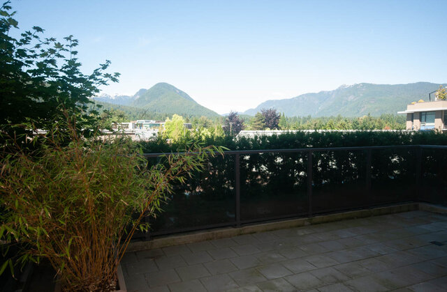 The balcony features a metal railing, greenery, and a view of mountains and trees. - 203 -2785 Library Lane, North Vancouver