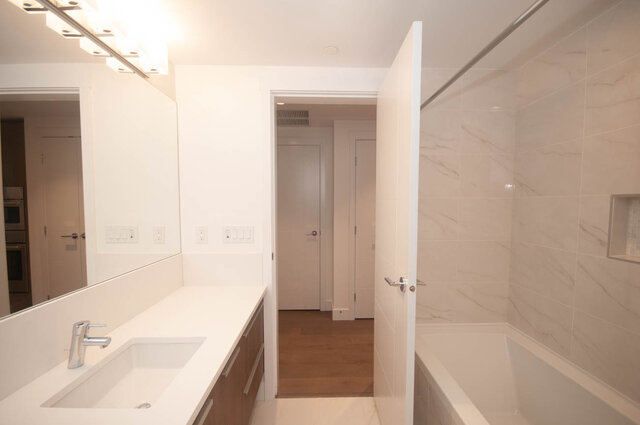 This is a bathroom featuring a white countertop with a sink, a mirror, marble tile walls, a light fixture, and a bathtub.