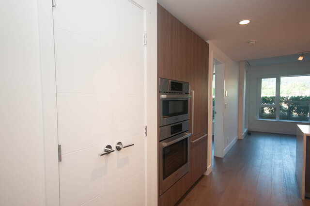 The kitchen features stainless steel built-in ovens, wooden cabinets, hardwood floors, and recessed ceiling lighting.