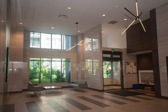 The lobby features large windows, a seating area with a sofa and coffee table, modern light fixtures, and glass entrance door