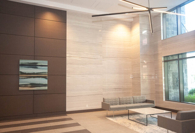 The lobby features a sofa, coffee table, artwork on the wall, large windows, and a modern light fixture. - 203 -2785 Library Lane, North Vancouver