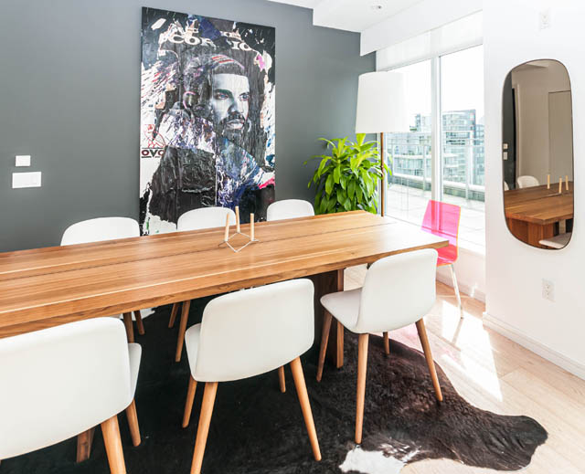 Furnished dining area with modern chairs, wooden table, cowhide rug, city view, and abstract wall art.