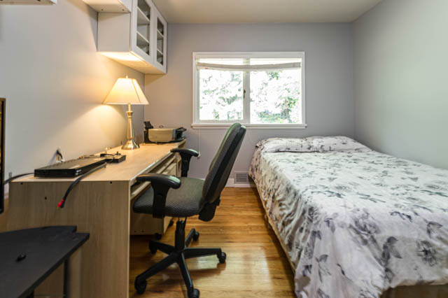 Bright bedroom with wooden floors and a desk setup, featuring a window with a view. - 1249 Nepal Crescent, West Vancouver