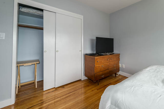 Bright bedroom with hardwood floors, a TV on a wooden dresser, and a neatly made bed. - 1249 Nepal Crescent, West Vancouver