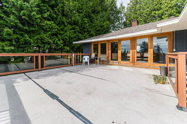 Spacious patio with wooden railings and glass panels, surrounded by lush greenery. - 1249 Nepal Crescent, West Vancouver